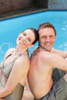 Couple sitting beside the swimming pool back to back