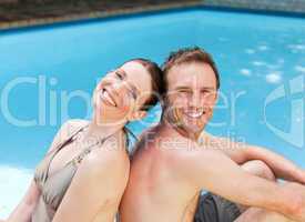 Couple sitting beside the swimming pool back to back