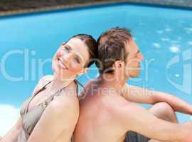 Couple sitting beside the swimming pool back to back