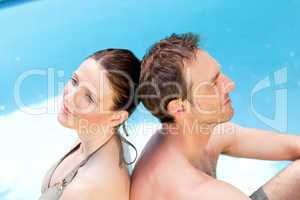 Couple sitting beside the swimming pool back to back