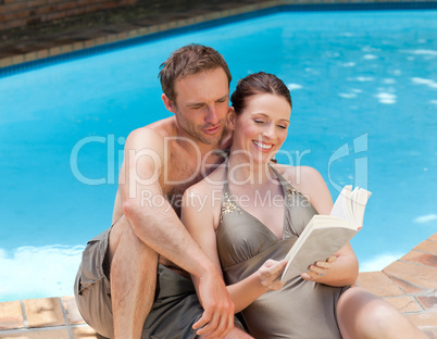 Couple reading a book beside the swimming pool
