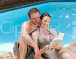 Couple reading a book beside the swimming pool