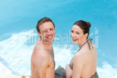 Couple looking at the camera beside the swimming pool