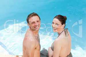 Couple looking at the camera beside the swimming pool