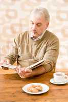 Senior mature man reading book having coffee