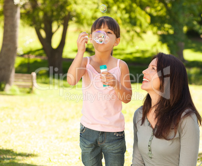 Girl blowing bubbles with her mother in the park