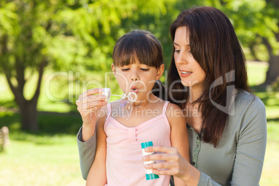 Girl blowing bubbles with her mother in the park