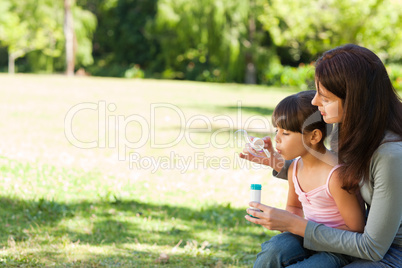 Girl blowing bubbles with her mother in the park