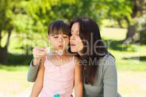 Girl blowing bubbles with her mother in the park