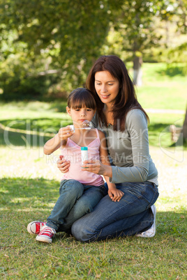 Girl blowing bubbles with her mother in the park