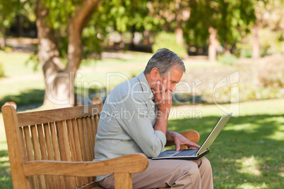 Elderly man working on his laptop in the park