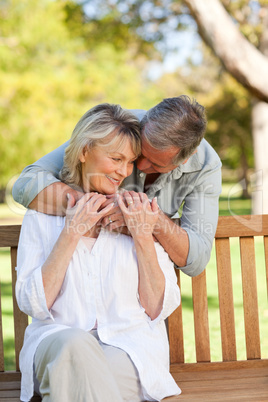 Elderly man hugging his wife who is on the bench