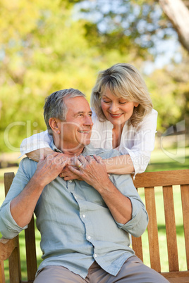 Senior woman hugging her husband who is on the bench