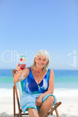 Elderly woman drinking a cocktail on the beach