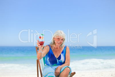 Elderly woman drinking a cocktail on the beach