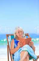 Senior woman reading a book on the beach