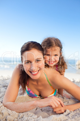 Mother and daughter lying down on the beach