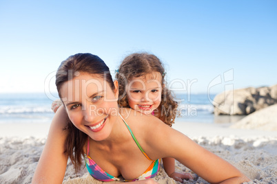 Mother and daughter lying down on the beach