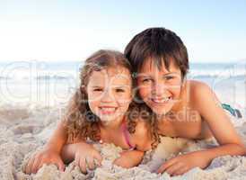 Little boy and his sister lying down on the beach