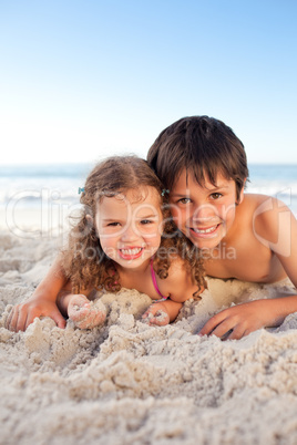 Little boy and his sister lying down on the beach