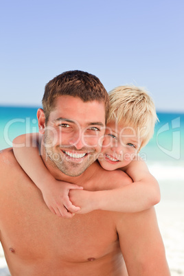 Smiling father having son a piggyback at the beach