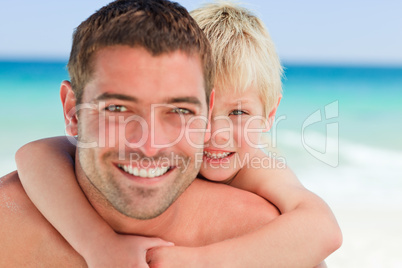 Smiling father having son a piggyback at the beach