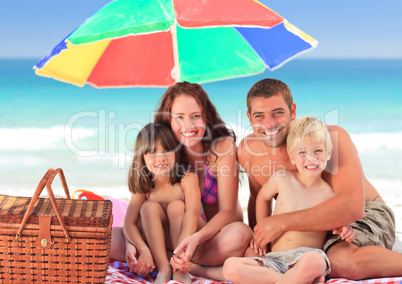 Family picnicking under a sol umbrella on the beach