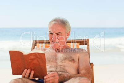 Senior man reading a book at the beach