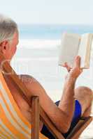 Senior man reading a book at the beach