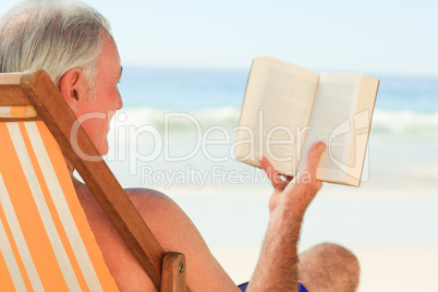 Senior man reading a book at the beach Senior man reading a book at the beach