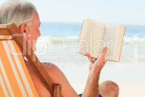 Senior man reading a book at the beach