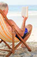 Senior man reading a book at the beach