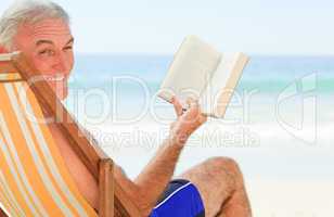 Senior man reading a book at the beach