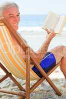 Senior man reading a book at the beach