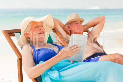 Woman reading a book while her husband is sleeping at the beach