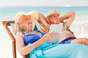 Woman reading a book while her husband is sleeping at the beach