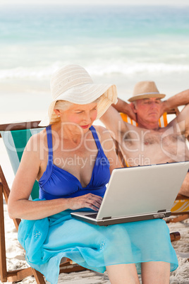 Woman working on her laptop while her husband is sleeping at the