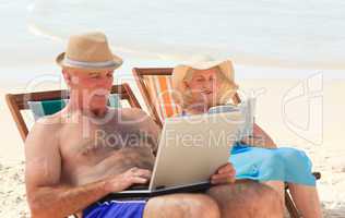 Man working on his laptop while his wife is reading at the beach