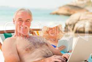 Man working on his laptop while his wife is reading at the beach