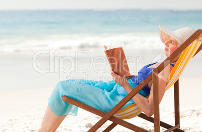 Elderly woman reading a book at the beach