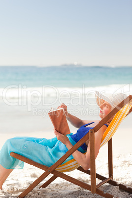 Elderly woman reading a book at the beach