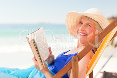 Elderly woman reading a book at the beach