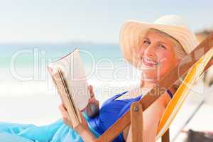 Elderly woman reading a book at the beach