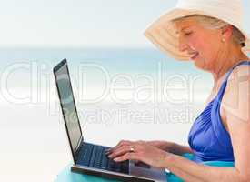 Happy woman working on her laptop at the beach