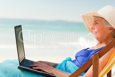 Happy woman working on her laptop at the beach