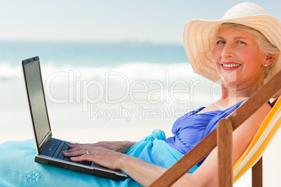 Happy woman working on her laptop at the beach