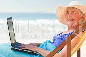 Happy woman working on her laptop at the beach
