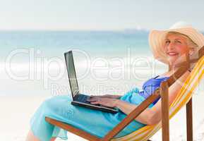 Happy woman working on her laptop at the beach