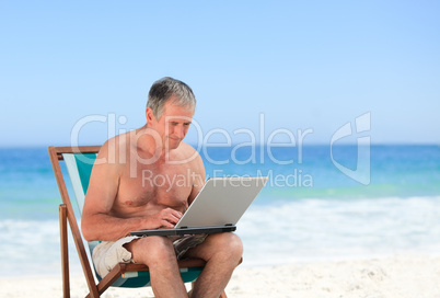 Retired man working on his laptop on the beach