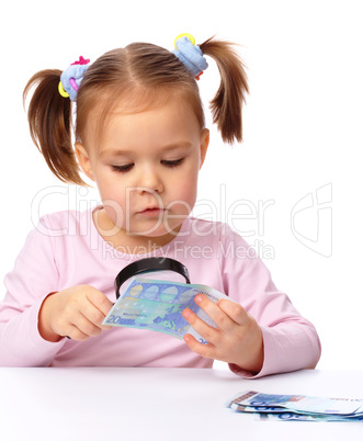 Girl is looking at euro banknote using magnifier